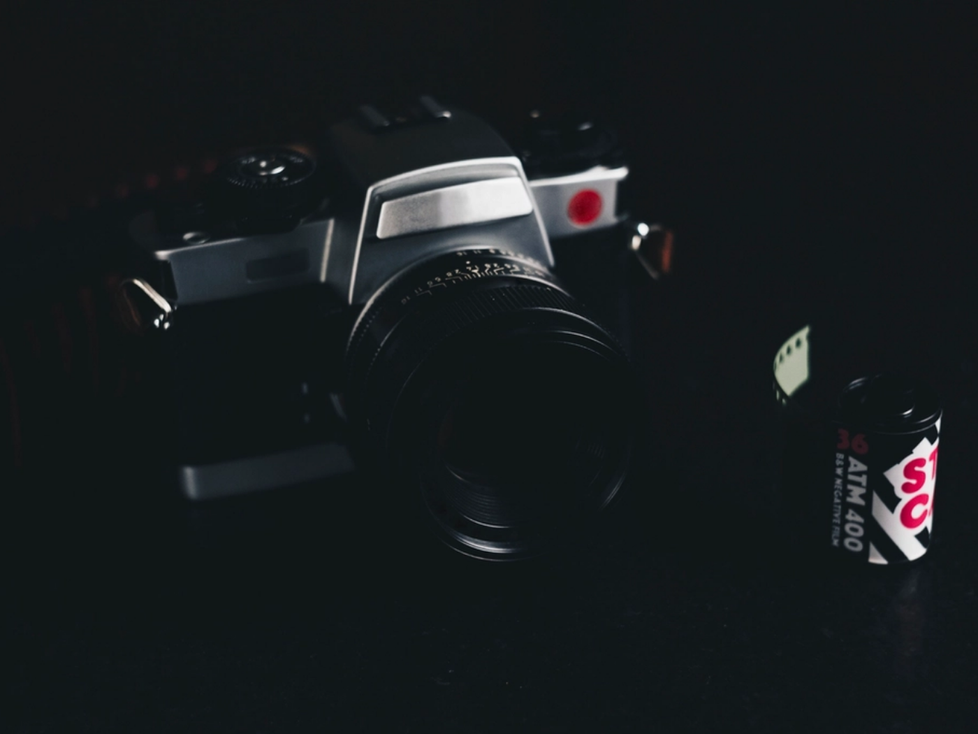 Analoge Kamera mit Objektiv neben einer Filmpatrone auf dunklem Untergrund